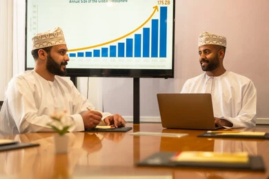 Studying statistical data, analyzing charts, conducting job interviews, concluding successful new business deals between businessmen, two Omani Arab Gulf men wearing traditional attire discussing their work tasks, expanding business fields, partnership in business and engineering projects.