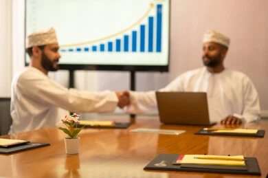 Successful new business deals between businessmen, conducting a job interview, two Omani Arab Gulf men wearing traditional attire shaking hands, expanding business fields, partnership in business and engineering projects, studying statistical data, analyzing charts.