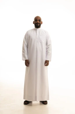 مفهوم الرجولة والثقة بالنفس، الاهتمام بالمظهر الخارجي والأناقة، بورتريه لرجل عربي خليجي سعودي يرتدي الثوب التقليدي ينظر بتعابير السرور، الوقوف باستقامة وثبات، صورة الجسم بالطول الكامل، خلفية بيضاء