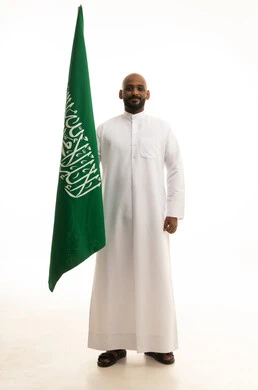 بورتريه لرجل عربي سعودي خليجي مبتسم يرتدي الثوب التقليدي يحمل بيده علم السعودية , يوم العلم 11مارس، الاحتفال باليوم الوطني 8 ربيع الأول, الفخر و الاعتزاز بالانتماء للمملكة, ذكرى العيد الوطني السعودي, خلفية بيضاء