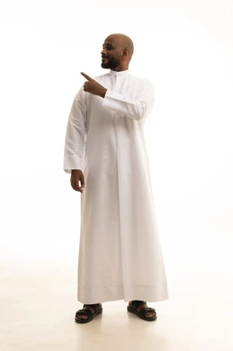 Looking at the camera with gestures of confidence, signals and hand movements indicating this place (here), pinpointing a specific object, a portrait of a smiling Arab Saudi Gulf man wearing a ghutrah and traditional thobe pointing with his index finger, attention to external appearance, full-body shot, white background.