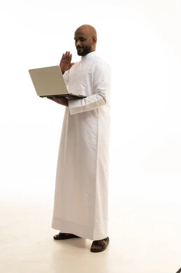 عقد إجتماع عمل عبر الإنترنت، تصفح برامج التواصل الاجتماعي, إستخدام الحاسوب المحمول لإنجاز المهام، بورتريه لرجل عربي خليجي سعودي يرتدي الثوب التقليدي يستخدم جهاز اللابتوب، تطور التكنولوجيا والأجهزة التقنية، خلفية بيضاء