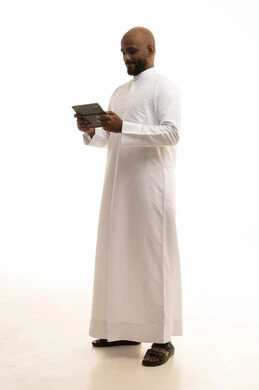 Gestures of joy and happiness, using a modern and advanced technical device, chatting with friends and relatives via the tablet, an Arab Gulf Saudi man wearing traditional attire holding the tablet in his hand, white background.
