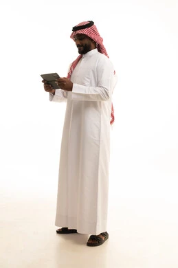 A portrait of a Saudi Arabian Gulf man wearing traditional attire and a ghutrah, holding a tablet in his hand, using a modern and advanced technological device, chatting with friends and relatives via the tablet, gestures of joy and happiness, white background.