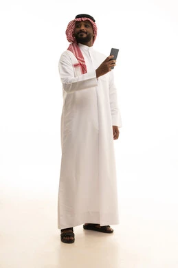 The integration of modern technologies into daily life, chatting with friends and relatives via mobile, gestures of joy and happiness, an Arab Gulf Saudi man wearing traditional attire and a ghutrah holding a mobile phone in his hand, white background.