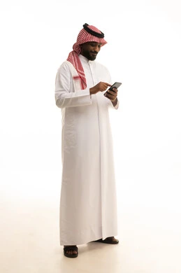Making phone calls, using a modern and advanced technical device, chatting with friends and relatives via mobile, gestures of joy and happiness, an Arab Gulf Saudi man wearing traditional attire and a ghutrah holding a mobile phone in his hand, white background.