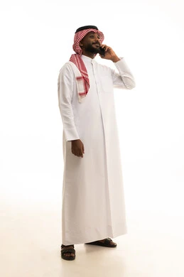 Making phone calls, using a modern and advanced technical device, chatting with friends and relatives via mobile, gestures of joy and happiness, an Arab Gulf Saudi man wearing traditional attire and a headscarf holding a mobile phone in his hand, white background.