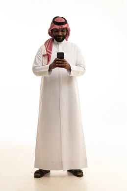 Making phone calls, using a modern and advanced technical device, chatting with friends and relatives via mobile, gestures of joy and happiness, an Arab Gulf Saudi man wearing traditional attire and a ghutrah holding a mobile phone in his hand, white background.