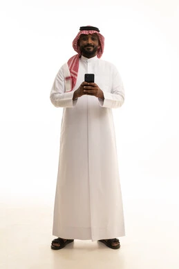 Making phone calls, using a modern and advanced technical device, chatting with friends and relatives via mobile, gestures of joy and happiness, an Arab Gulf Saudi man wearing traditional attire and a ghutrah holding a mobile phone in his hand, white background.