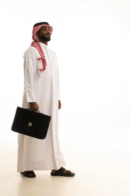 The concept of business and project management, walking and going to a place, paying attention to external appearance and elegance, a portrait of a smiling Arab Gulf Saudi businessman wearing traditional attire and a shemagh, holding a black leather bag in his hand, looking at the camera with gestures of cheerfulness and joy, full-body image, white background.