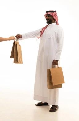 Reliable shipping and delivery process, fast delivery services, ordering and receiving delivery, portrait of an Arab Saudi Gulf man wearing traditional attire and a ghutrah working in delivering orders and goods to customers, online shopping and online orders, white background. Reliable shipping and delivery process, fast delivery services, ordering and receiving delivery, portrait of an Arab Saudi Gulf man wearing traditional attire and a ghutrah working in delivering orders and goods to customers, online shopping and online orders, white background.