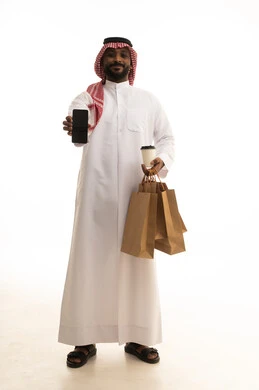 دمج التقنيات الحديثة فى الحياه اليوميه ، عملية شحن وتوصيل موثوقه, خدمات التوصيل السريع, طلب وإستلام الدليفري, بورتريه لرجل عربي سعودي خليجي يرتدي الزى التقليدي والشماغ يمسك بيده الجوال يعمل في توصيل الطلبات والبضائع للزبائن, التسوق الالكتروني وطلبات اونلاين, خلفيه بيضاء