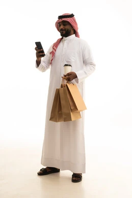 Browsing social media, reliable shipping and delivery process, fast delivery services, ordering and receiving delivery, a portrait of an Arab Saudi Gulf man wearing traditional attire and a ghutrah holding a mobile phone working in delivering orders and goods to customers, online shopping and online orders, white background.