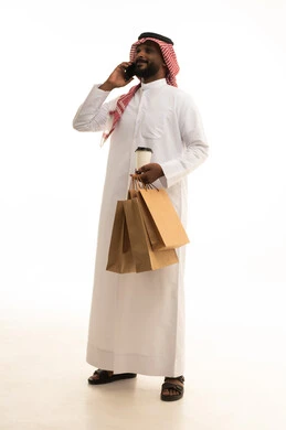Integrating modern technologies into daily life, reliable shipping and delivery processes, fast delivery services, ordering and receiving delivery, a portrait of an Arab Saudi Gulf man wearing traditional attire and a ghutrah holding a mobile phone working in delivering orders and goods to customers, online shopping and online orders, white background.