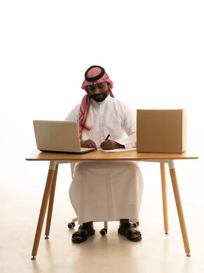 The concept of electronic marketing and online orders, taking important notes, Saudi professions and jobs, a portrait of a Saudi Gulf Arab man wearing traditional attire and a ghutrah using a laptop with shopping bags in front of him, browsing social media, using modern technological devices, working remotely, white background.