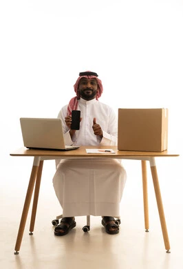 A blank black screen display, browsing social media, using modern technology devices, remote work, the concept of electronic marketing and online orders, a portrait of a Saudi Arabian Gulf man wearing traditional attire and a ghutrah using a laptop, pointing to a mobile phone in front of him with shopping bags, white background. A blank black screen display, browsing social media, using modern technology devices, remote work, the concept of electronic marketing and online orders, a portrait of a Saudi Arabian Gulf man wearing traditional attire and a ghutrah using a laptop, pointing to a mobile phone in front of him with shopping bags, white background.