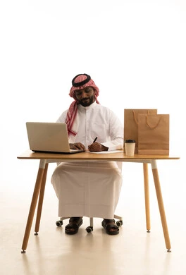 The concept of electronic marketing and online orders, taking important notes, Saudi professions and jobs, a portrait of a Saudi Gulf Arab man wearing traditional attire and a ghutrah using a laptop with shopping bags in front of him, browsing social media, using modern technological devices, working remotely, white background. The concept of electronic marketing and online orders, taking important notes, Saudi professions and jobs, a portrait of a Saudi Gulf Arab man wearing traditional attire and a ghutrah using a laptop with shopping bags in front of him, browsing social media, using modern technological devices, working remotely, white background.