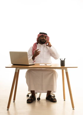 Checking on family and friends, using modern technology devices, working remotely, displaying a blank black screen on the mobile, holding a business meeting via laptop, a portrait of a Saudi Arabian Gulf man wearing traditional attire and a ghutrah using a laptop, browsing social media, white background.
