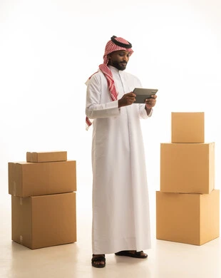 Owning a new home and family stability, using modern technological devices, arranging and organizing the house, a portrait of a Saudi Arabian Gulf man wearing traditional attire and a ghutrah, carrying boxes of household items while holding a tablet in his hand, modern housing and ownership, full-body image, white background.