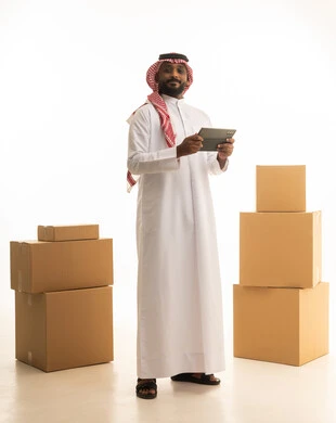 Using modern technological devices, arranging and organizing the home, a portrait of a Saudi Arabian Gulf man wearing traditional attire and a ghutrah, carrying boxes of household items while holding a tablet in his hand, owning a new home and family stability, modern housing and ownership, full-body image, white background.
