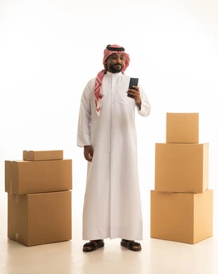 بورتريه لرجل عربي خليجي سعودي يرتدي الزى التقليدي والشماغ  يقوم بنقل صناديق الأغراض المنزلية يمسك بيده جهاز الجوال ، امتلاك سكن جديد والاستقرار العائلي، اسكان وتمليك حديث ، استخدام الهاتف المحمول ، اجراء مكالمه هاتفيه،  ترتيب وتنظيم المنزل،صورة الجسم بالطول الكامل، خلفية بيضاء