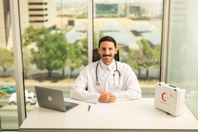 متابعة حالات المرضى عبر الاجهزة و التقنيات الحديثة, استخدام حقيبة الاسعافات الاوليه و جهاز الحاسوب في الطب، طبيب عربي خليجي سعودي مبتسم يرتدي المعطف الأبيض ينظر إلى الكاميرا بإيماءات الثقة بالنفس، تسجيل التقارير والحالات الصحيه