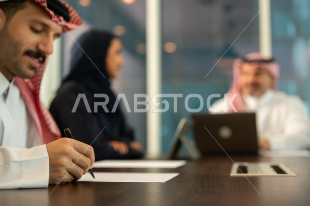 Writing and taking notes, discussing work plans, providing a comfortable work environment, the concept of team spirit and collective achievement, developing strategies and businesses, success and achieving goals, using modern devices and technologies to accomplish office tasks, Saudi and Gulf Arab employees in a meeting at the company headquarters