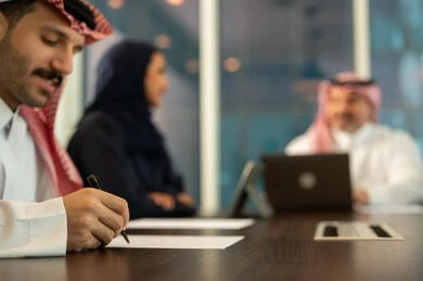Writing and taking notes, discussing work plans, providing a comfortable work environment, the concept of team spirit and collective achievement, developing strategies and businesses, success and achieving goals, using modern devices and technologies to accomplish office tasks, Saudi and Gulf Arab employees in a meeting at the company headquarters