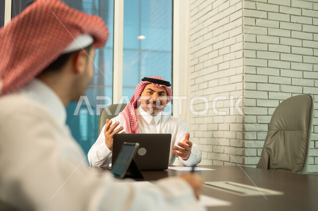 استخدام الحاسب والتقنية في مجال الاعمال، بيئة العمل المريحة في الشركات السعودية، الحوار و النقاش بين الزملاء، تبادل الخبرات والمعلومات لتحقيق الاهداف, موظفان عربيان خليجيان سعوديان يقومان بالعمل ومشاركة الأفكار داخل مقر الشركة