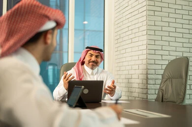 استخدام الحاسب والتقنية في مجال الاعمال، بيئة العمل المريحة في الشركات السعودية، الحوار و النقاش بين الزملاء، تبادل الخبرات والمعلومات لتحقيق الاهداف, موظفان عربيان خليجيان سعوديان يقومان بالعمل ومشاركة الأفكار داخل مقر الشركة