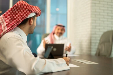 تبادل الخبرات والمعلومات لتحقيق الاهداف, استخدام الحاسب والتقنية في مجال الاعمال، بيئة العمل المريحة في الشركات السعودية، الحوار و النقاش بين الزملاء، موظفان عربيان خليجيان سعوديان يقومان بالعمل ومشاركة الأفكار داخل مقر الشركة