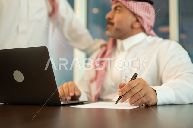 Using computers and technology in business, comfortable work environment in Saudi companies, dialogue and discussion between colleagues, exchange of experiences and information to achieve goals, two Saudi Gulf Arab employees working and sharing ideas within the company's headquarters