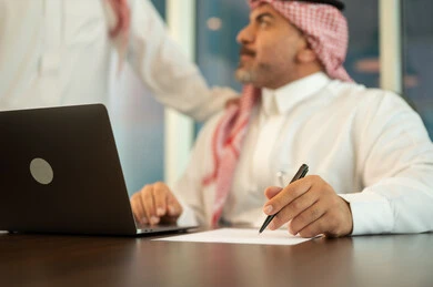 Using computers and technology in business, comfortable work environment in Saudi companies, dialogue and discussion between colleagues, exchange of experiences and information to achieve goals, two Saudi Gulf Arab employees working and sharing ideas within the company's headquarters