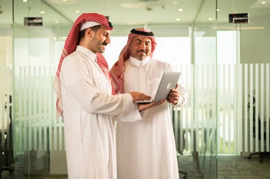 تبادل الخبرات والمعلومات لتحقيق الاهداف, استخدام الحاسب والتقنية في مجال الاعمال، بيئة العمل المريحة في الشركات السعودية، الحوار و النقاش بين الزملاء، موظفان عربيان خليجيان سعوديان يقومان بالعمل ومشاركة الأفكار داخل مقر الشركة