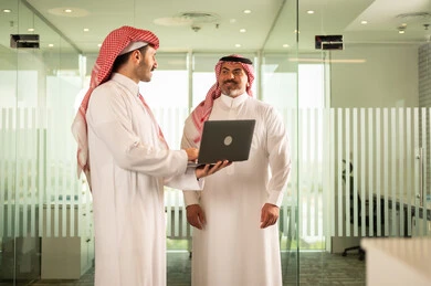 استخدام الحاسب والتقنية في مجال الاعمال، بيئة العمل المريحة في الشركات السعودية، الحوار و النقاش بين الزملاء، تبادل الخبرات والمعلومات لتحقيق الاهداف, موظفان عربيان خليجيان سعوديان يقومان بالعمل ومشاركة الأفكار داخل مقر الشركة
