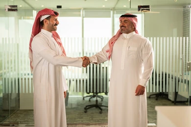 Agreement and partnership on business and commercial projects, acquaintance, friendships and building social relationships, new successful business deals between businessmen, two Saudi Gulf Arab men shaking hands inside the company headquarters with gestures of happiness and pleasure