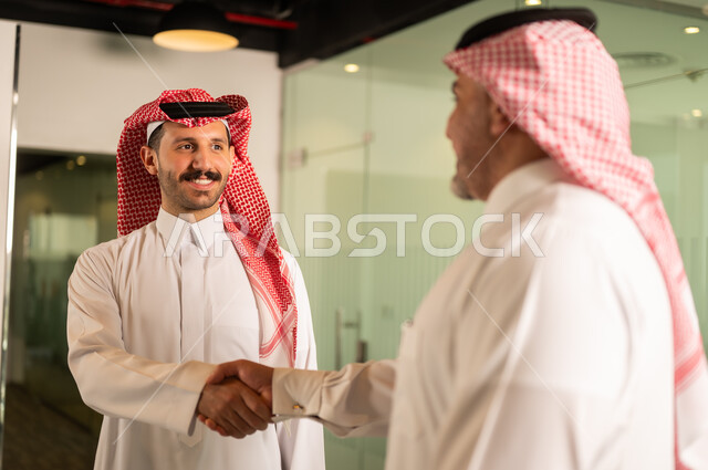الاتفاق والشراكة على الأعمال والمشاريع التجارية، تعارف وصداقات وبناء علاقات اجتماعية، صفقات عمل جديدة ناجحة بين رجال الأعمال، رجلان عربيان خليجيان سعوديان يقومان بمصافحة بعضهما داخل ممقر الشركة بإيماءات السعادة والسرور