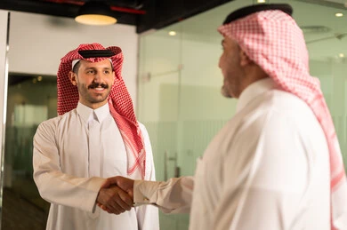 Agreement and partnership on business and commercial projects, acquaintance, friendships and building social relationships, new successful business deals between businessmen, two Saudi Gulf Arab men shaking hands inside the company headquarters with gestures of happiness and pleasure