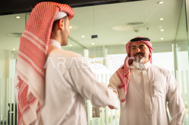 صفقات عمل جديدة ناجحة بين رجال الأعمال، الاتفاق والشراكة على الأعمال والمشاريع التجارية، تعارف وصداقات وبناء علاقات اجتماعية، صورة مقربة لرجلين عربيين خليجيين سعوديين يقومان بمصافحة بعضهما داخل مقر الشركة 