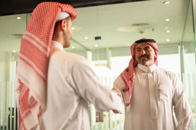 Successful new business deals between businessmen, agreement and partnership on business and commercial projects, acquaintance, friendships and building social relationships, a close-up photo of two Saudi Arabian Gulf men shaking hands inside the company headquarters