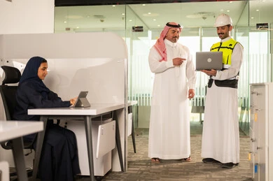 تصميم وتخطيط المخططات المعمارية عبر الحاسوب المحمول، متابعة تنفيذ الخطط الهندسية، الشركات المختصة بورشات البناء والمقاولات، رجل أعمال عربي خليجي سعودي يرتدي الشماغ ومهندس يرتدي الخوذة وسترة الحماية يقومان بالمناقشة وتبادل الخبرات، استخدام جهاز تقني حديث