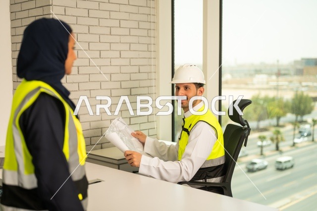 Completion of engineering works, unity and teamwork to achieve the company's goals, companies specialized in construction workshops and contracting, design and planning of architectural plans, an Arab Gulf engineer and engineer from Saudi Arabia wearing safety vests are discussing and exchanging experiences.