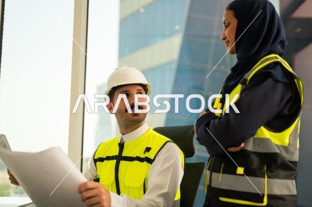 Completion of engineering works, unity and teamwork to achieve the company's goals, companies specialized in construction workshops and contracting, design and planning of architectural plans, an Arab Gulf engineer and engineer from Saudi Arabia wearing safety vests are discussing and exchanging experiences.
