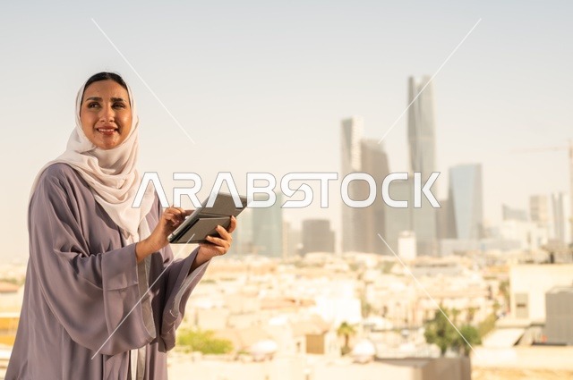 جهاز تقني حديث و متطور،تصفح الانترنت و مواقع التواصل الاجتماعي عبر جهاز التابليت ،سيدة عربية خليجية سعودية ترتدي العباءة تقوم باستخدام الجهاز اللوحي بايماءات السعادة والسرور،الخروج في الهواء الطلق،التواصل مع الاهل و الاصدقاء