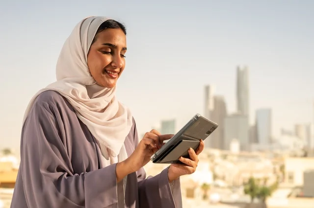 التواصل مع الاهل و الاصدقاء ،جهاز تقني حديث و متطور،تصفح الانترنت و مواقع التواصل الاجتماعي عبر جهاز التابليت ،صورة  مقربة لشابة عربية خليجية سعودية ترتدي العباءة تقوم باستخدام الجهاز اللوحي بايماءات السعادة والسرور،الخروج في الهواء الطلق