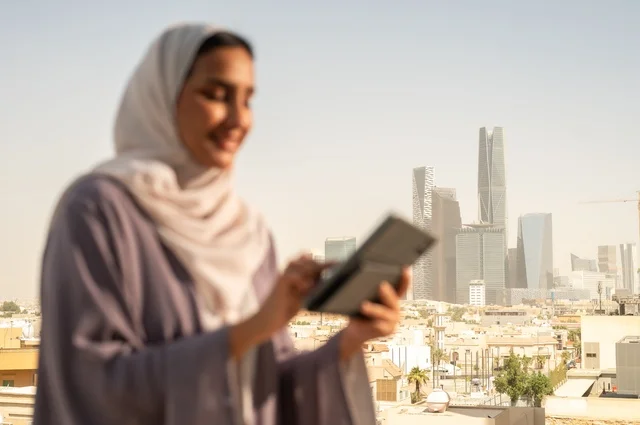 التواصل مع الاهل و الاصدقاء ،جهاز تقني حديث و متطور،تصفح الانترنت و مواقع التواصل الاجتماعي عبر جهاز التابليت ،صورة  مقربة لشابة عربية خليجية سعودية ترتدي العباءة تقوم باستخدام الجهاز اللوحي بايماءات السعادة والسرور،الخروج في الهواء الطلق