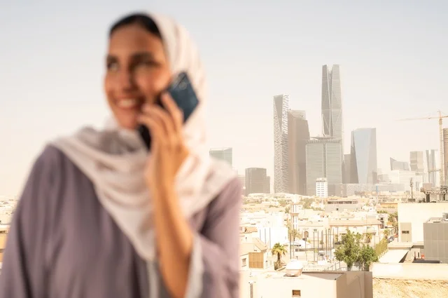 Making a phone call via a mobile device, a close-up image of a Gulf Arab Saudi woman wearing an abaya using a mobile phone with gestures of happiness and joy, going outdoors, communicating with family and friends.