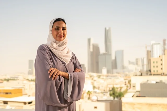 مفهوم الاناقة والاهتمام بالمظهر الخارجي، شابة عربية خليجية سعودية ترتدي العباءة تقف بايدي متقاطعة ، النظر الى شيء ما بايماءات السعادة والسرور،الخروج في الهواء الطلق