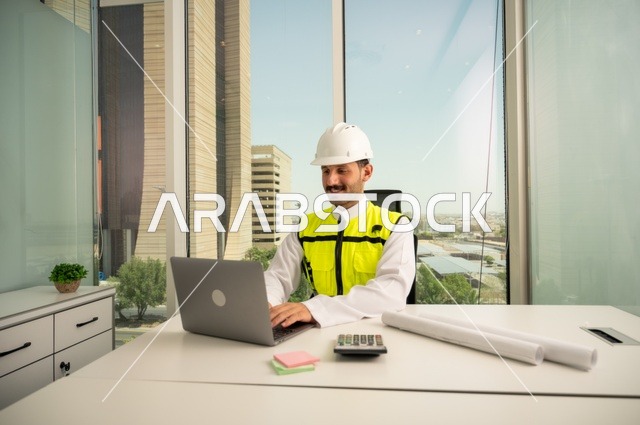 Integrating technology with engineering to complete construction drawings, review and audit engineering plans, engineering and construction concept, Saudi Arabian Gulf engineer wearing traditional thobe, jacket and work helmet sitting at desk working on laptop