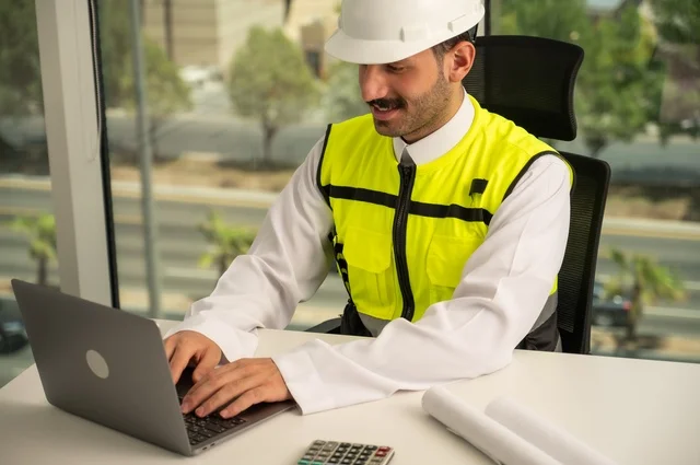   مهارة وسرعة الأيدي في الكتابة، تدقيق ومراجعة الخطط الهندسية, لإكمال رسم مخطوطات البناء دمج التكنولوجيا مع الهندسة ،مفهوم الهندسة والإنشاءات، مهندس عربي خليجي سعودي يرتدي الثوب التقليدي والسترة الخاصة بالعمل يجلس على المكتب ويعمل على الحاسوب المحمول 